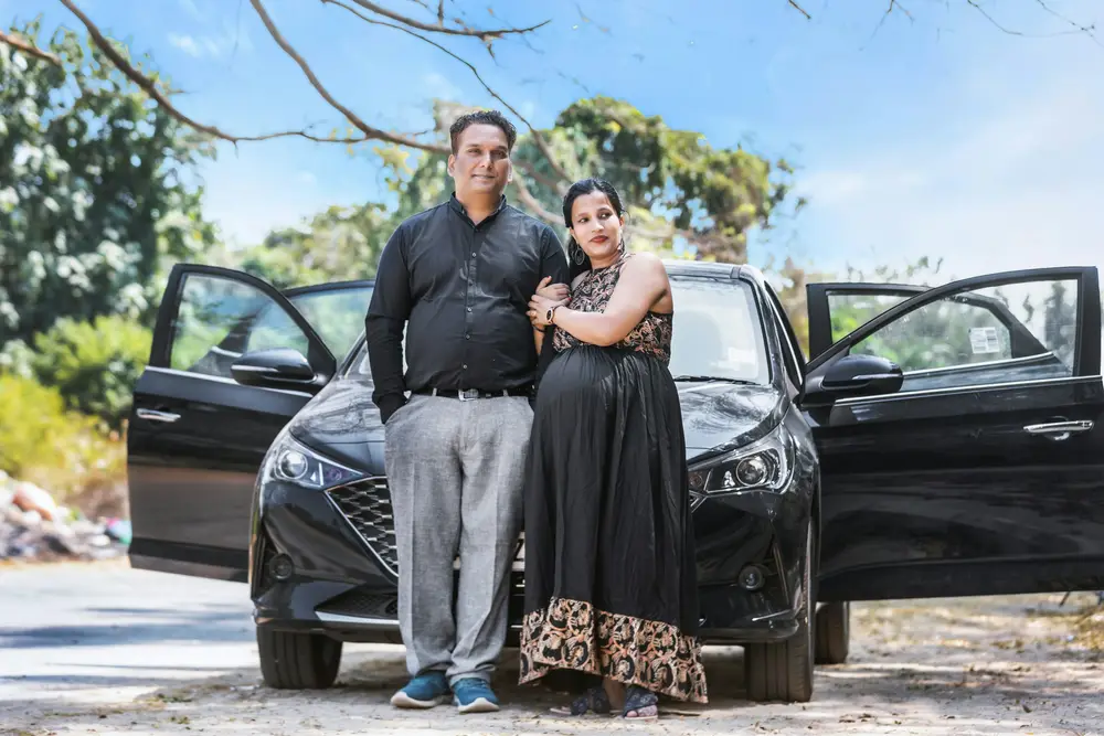 A smiling couple standing in front of their new black car